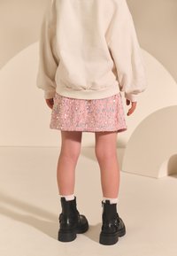 Enfant portant un sweat-shirt blanc et une jupe à paillettes rose. Bottines noires à semelles épaisses et chaussettes rose pâle.