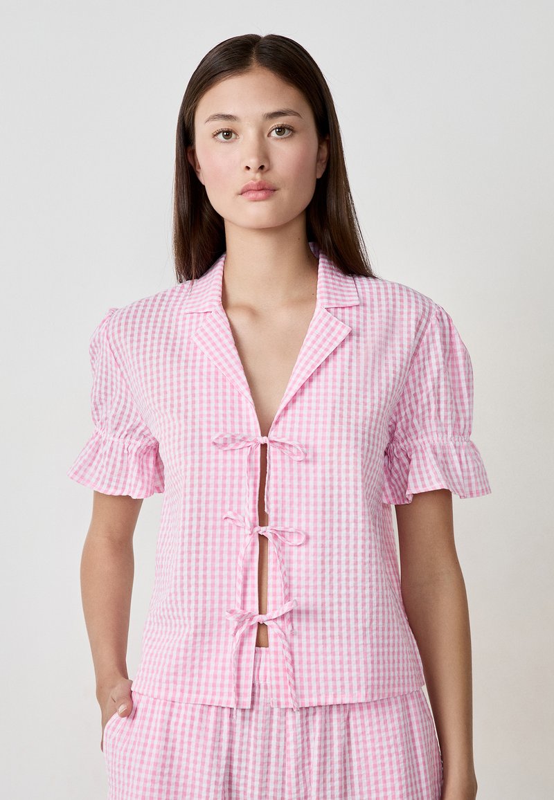 Pink gingham top with short ruffled sleeves, open front fastened by ties, and soft texture. Designed in a casual, relaxed fit.
