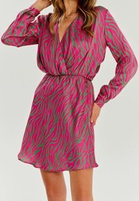 Mujer con un vestido envolvente de manga larga, en estampado de cebra rosa y verde, con cintura ajustada y falda corta.