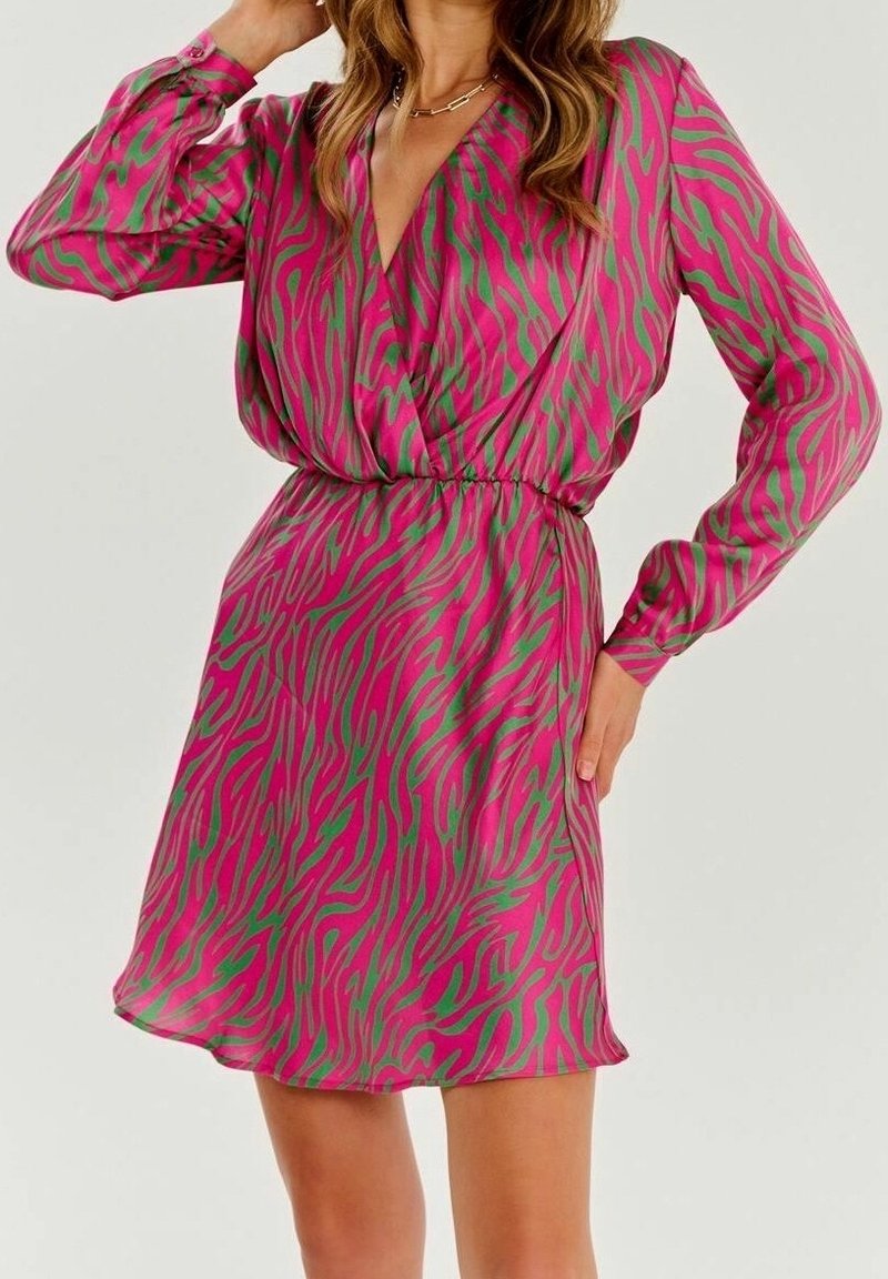 Mujer con un vestido envolvente de manga larga, en estampado de cebra rosa y verde, con cintura ajustada y falda corta.