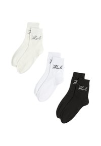 Tre par ankelstrømper i hvid, off-white og sort med "Karl" broderet nær manchetten i sølvtråd.