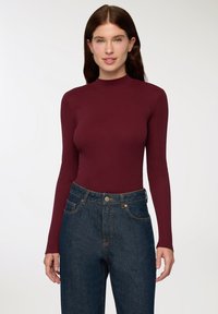 Body a maniche lunghe bordeaux in tessuto a costine abbinato a jeans blu a vita alta con chiusura a bottone e tasche frontali.