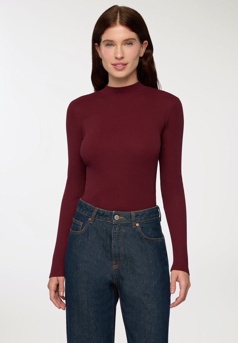 Body a maniche lunghe bordeaux in tessuto a costine abbinato a jeans blu a vita alta con chiusura a bottone e tasche frontali.