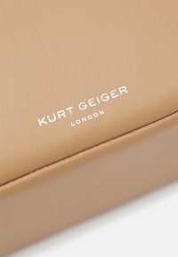 Accessorio in pelle beige con una texture liscia, caratterizzato da testo bianco impresso che recita "KURT GEIGER LONDON" sulla superficie.