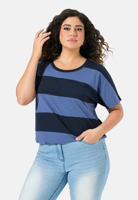 Camiseta de manga corta a rayas en azul oscuro y claro alternando. Presenta un escote redondo y un corte relajado. Combinada con jeans de un azul claro.
