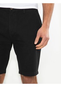 Shorts de mezclilla negra con cierre de botón, bolsillos frontales y dobladillos enrollados. La tela tiene una textura suave y un detalle de costura mínimo.