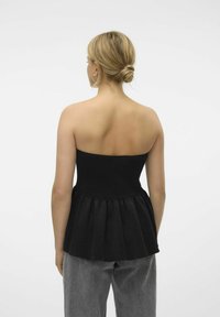 Svart strapless topp med en åtsittande kropp och en veckad peplum-kant. Tyget verkar slätt och texturerat, kombinerat med grå byxor.