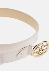 Biały pasek z tkaniny o subtelnym wzorze, z okrągłą złotą klamrą z logo. Gładka tekstura i regulowane zapięcie.