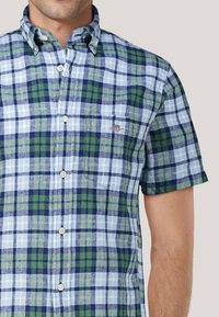 Kurzärmliges Hemd mit Knopfverschluss im Karomuster mit blauen, grünen und marineblauen Quadraten. Verfügt über eine Brusttasche und einen Button-down-Kragen.