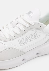 Weiße Sneaker aus einer Kombination von glattem Canvas und Wildledermaterialien, mit silberner "KARL"-Markierung und einer strukturierten, dicken Sohle.