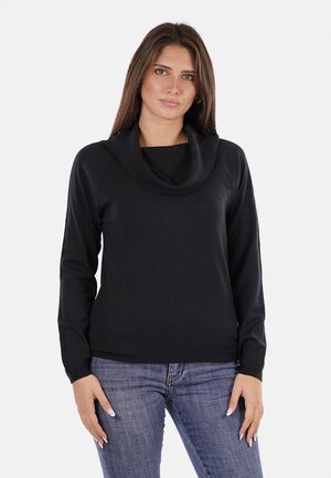 Pullover nera con colletto a scialle, maniche lunghe e vita aderente. Realizzata in un morbido tessuto testurizzato. Indossata con jeans blu.