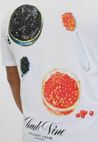 Valge T-särk, millel on värvilised illustratsioonid kaaviarist ringikujulistes taldrikutes, mustast ja punasest kaaviarist ning tekst "Cloud Nine Exclusive Caviar."