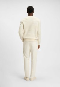 Hvid strikket sweater med teksturerede bølgemønstre, parret med cremefarvede skræddersyede bukser og lyse beige sneakers.
