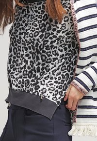 Top con stampa leopardata in bianco e nero con orlo scuro, abbinato a un cardigan a righe con un accento decorativo intrecciato e bordo frangiato.