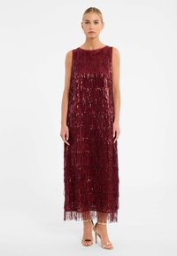 Bordeaux mouwloze jurk met franjes en pailletten, met een rechte silhouet. Gemaakt in combinatie met gouden sleehakken.