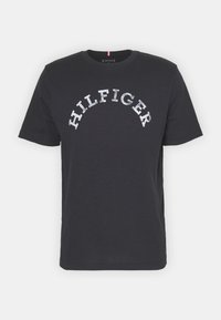 Camiseta de algodón en azul marino oscuro con mangas cortas, escote redondo y la marca "HILFIGER" impresa en plata a lo largo del pecho en un diseño arqueado.
