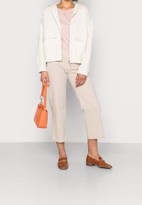 Lehká krémová bunda na zip s elastickými manžetami, v kombinaci s pruhovaným růžovým topem a béžovými zkrácenými kalhotami. Oranžová prošívaná kabelka a hnědé mokasíny.