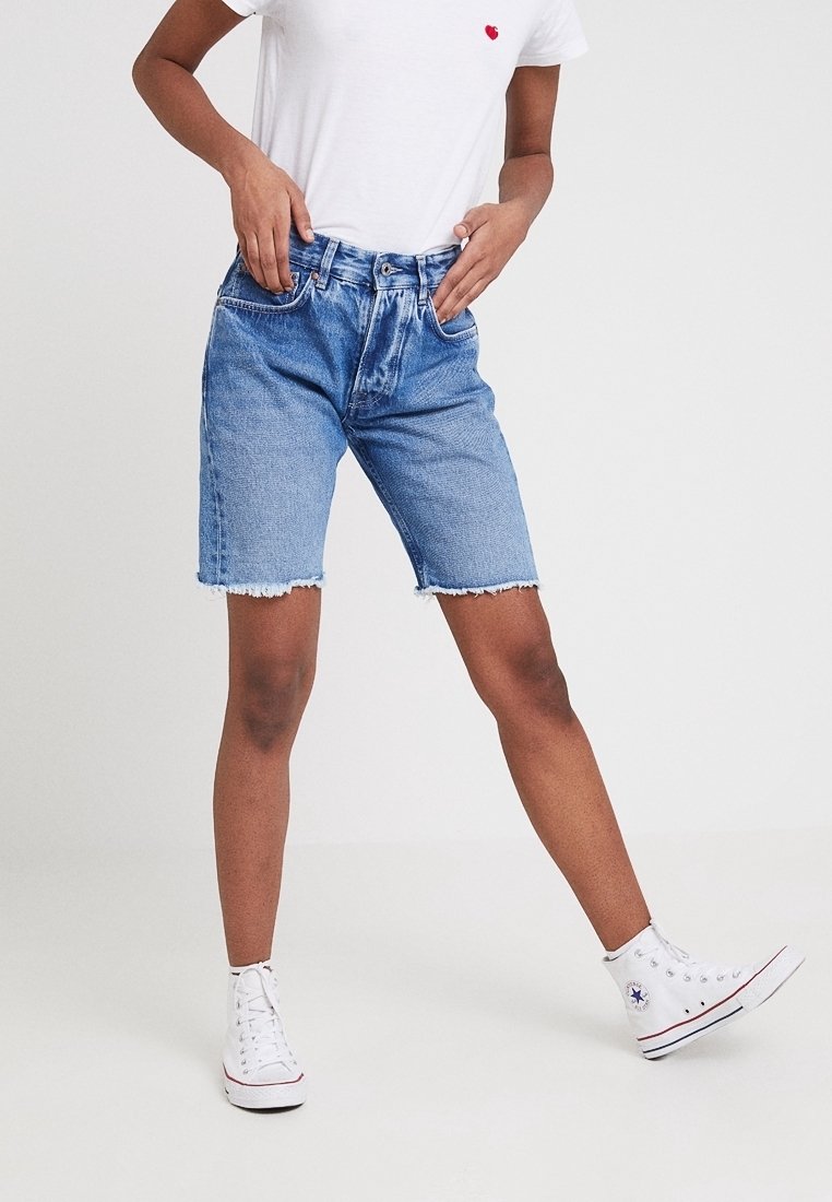 Jeansshorts i ljusblåtvättad tyg, fransad kant, femfickorsdesign, ihopparad med en vit t-shirt och vita högtoppsskor.