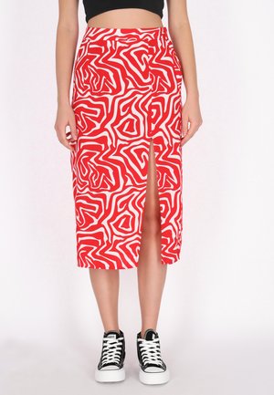 Kvinde iført et rød- og hvidt abstrakt mønstret midinederdel med frontslids, sort crop top og sorte høje sneakers med hvide snørebånd.
