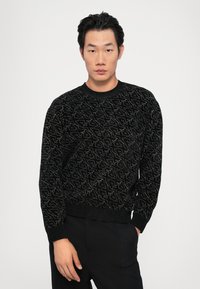 Pulover negru tricotat cu un model texturat în fir argintiu, având guler rotund și manșete și tiv cu model de jarfă.