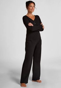 Zwarte loungewear set met een top met lange mouwen, een V-hals en knoopdetails, gecombineerd met losvallende broek, beide van zacht materiaal.