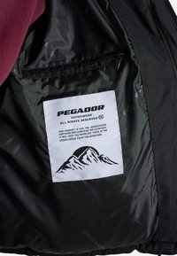 Černá vnitřní látková bunda s vínovým podšívkou. Obsahuje bílou etiketu s černým designem hory a textem o účelu produktu.