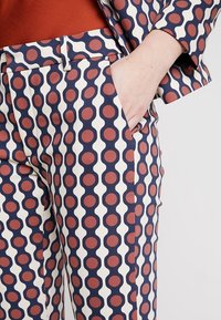 Pantalons à motifs en bleu marine, avec des motifs circulaires alternés en crème et maroon. Dispose d'une poche latérale et d'une silhouette ajustée.