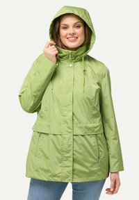 Ljusgrön, huvad regnjacka med dragkedja fram, elastiska dragsko, sidofickor och en något åtsittande midja för en figurnära look.