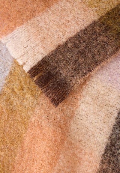 Gros plan d'un tissu doux et duveteux avec des sections superposées dans des tons chauds de beige, brun, crème et orange clair.