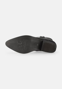 Suela de zapato de cuero negro con superficie texturizada, borde curvado y logo grabado. Presenta un tacón redondeado y un patrón de banda de rodadura prominente para mayor agarre.