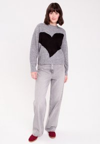 Grå sweater med et sort hjerte mønster, lange ærmer og rund hals, parret med lysegrå wide-leg jeans og burgundy sko.