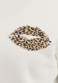 Tessuto bianco con una grafica di labbra a stampa leopardata testurizzata in tonalità di marrone, nero e oro. La stampa presenta un effetto invecchiato.
