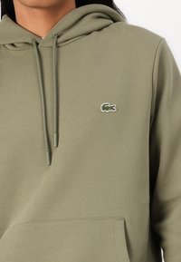Sweat à capuche vert olive en mélange de coton doux, avec une poche avant, un cordon de serrage à la capuche et un petit logo crocodile brodé sur la poitrine.