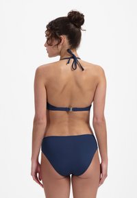 Set bikini blu navy con design a collo alto, caratterizzato da un fiocco sul retro e una chiusura in metallo argentato, realizzato in tessuto elastico e morbido.