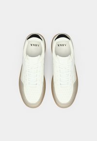 Λευκά αθλητικά παπούτσια με λείο δερμάτινο επάνω μέρος, διάτρητη μύτη, καφέ καουτσούκ σόλα, μαύρη λεπτομέρεια στη φτέρνα και λευκά επίπεδα κορδόνια.