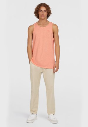 Light pink tank top with a rounded neck, paired with beige trousers and white sneakers. The fabric appears soft with a subtle texture.
