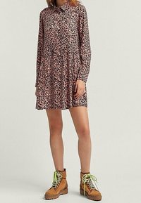 Vestido con estampado de leopardo rosa, de manga larga y con cuello, con falda acampanada. Combinado con botines marrones de tobillo que tienen cordones de neón verdes.