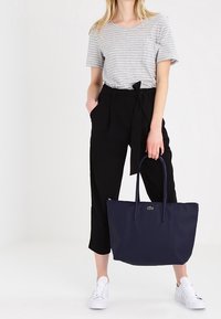Sac fourre-tout bleu marine avec deux longues anses, fabriqué en matériau texturé. T-shirt rayé gris et pantalon noir taille haute avec un nœud à l'avant.