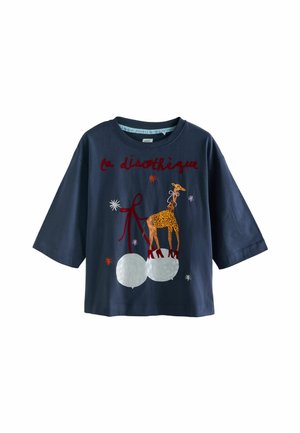 Jūros mėlynos medvilninės trumpomis rankovėmis marškinėliai, su išsiuvinėtu žirafa ant baltų kamuoliukų ir raudonuoju tekstu viršuje, supančių spalvingų žvaigždžių.