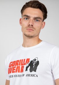 Camiseta de algodón blanca con un estampado gráfico en rojo y negro de un gorila y el texto "GORILLA WEAR ESTADOS UNIDOS DE AMÉRICA."