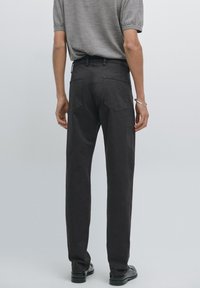 Pantaloni neri a gamba dritta con una texture liscia, dotati di due tasche posteriori e di un classico elastico in vita. Adatti per un abbigliamento casual.