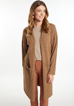 Bruine open voorkardigan met twee voorzakken, textuurstof, lange mouwen en een losse fit, gecombineerd met een beige top en bruine broek.