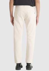 Pantalones de mezclilla beige claro con corte recto, que cuentan con bolsillos traseros, sutiles detalles de costura y que se combinan con botas negras brillantes.