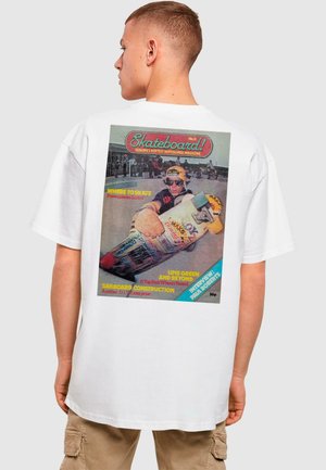 T-shirt blanche ornée d'un graphique rétro d'un magazine de skateboard au dos, avec du texte multicolore et une image d'un skateur.