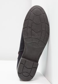 Semelle de chaussure en daim noir avec un dessous en caoutchouc texturé, présentant une prise à motif pour l'adhérence et un talon surélevé marqué de la taille "37".