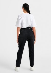 Černé vysoké džíny s rovný střih, s kapsami na zadní straně a texturovanou tkaninou. V kombinaci s volně střiženým bílým tričkem.