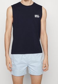 Marinblå ärmlös bomullstopp med rund halsringning, med en liten vit textgrafik på vänster bröst och en slät yta.