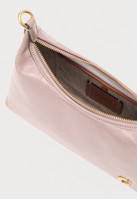 Ροζ δερμάτινο τσαντάκι χειρός με χρυσό φερμουάρ, χρυσές μεταλλικές λεπτομέρειες και ανοιχτόχρωμη υφασμάτινη επένδυση, που αποκαλύπτει οργανωμένο εσωτερικό και ετικέτα.