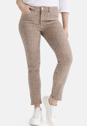 Leopardenmuster High-Waist-Jeans in beiger Farbe, mit tailliertem Schnitt, Fünf-Taschen-Design und knöchellangem Saum. Kombiniert mit weißen Sneakern.
