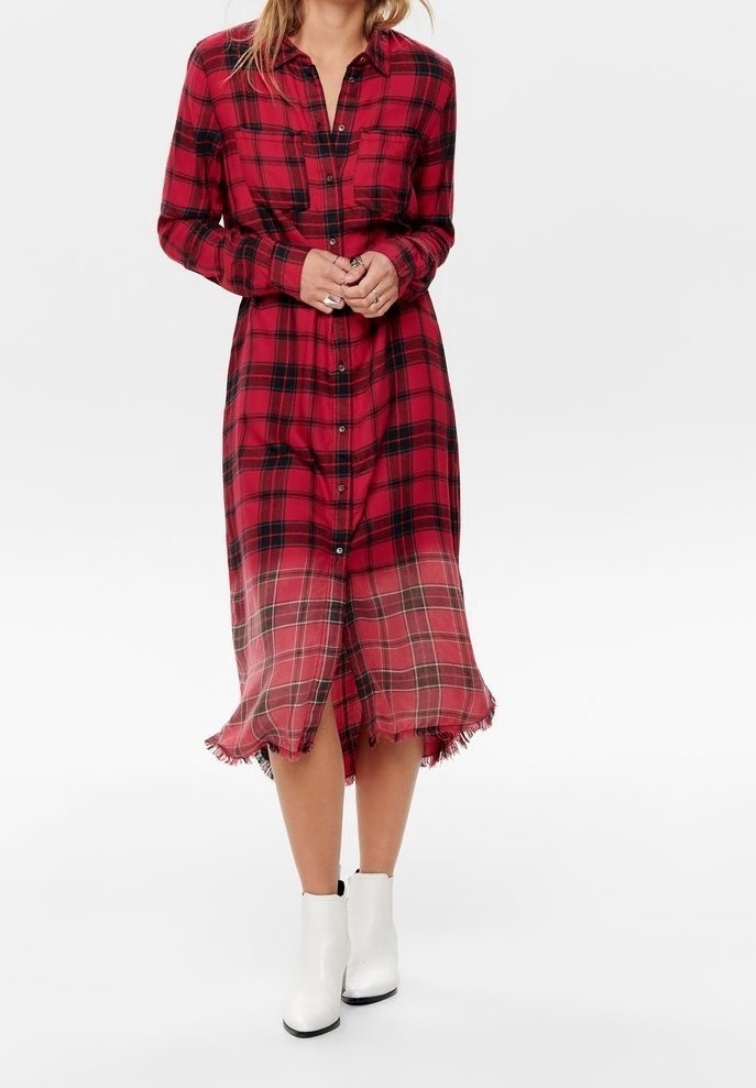 Femme portant une robe à carreaux rouge et noir boutonnée avec un ourlet effiloché et des bottines blanches, debout devant un fond uni.